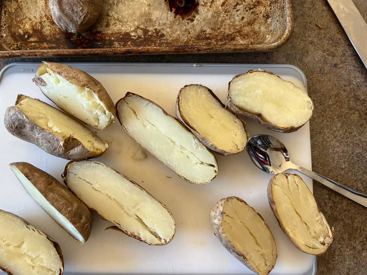Baked potatoes cut in half on cutting board.