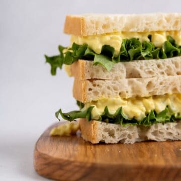 egg salad sandwich stacked on a wooden board.
