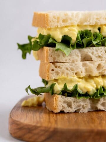 egg salad sandwich stacked on a wooden board.