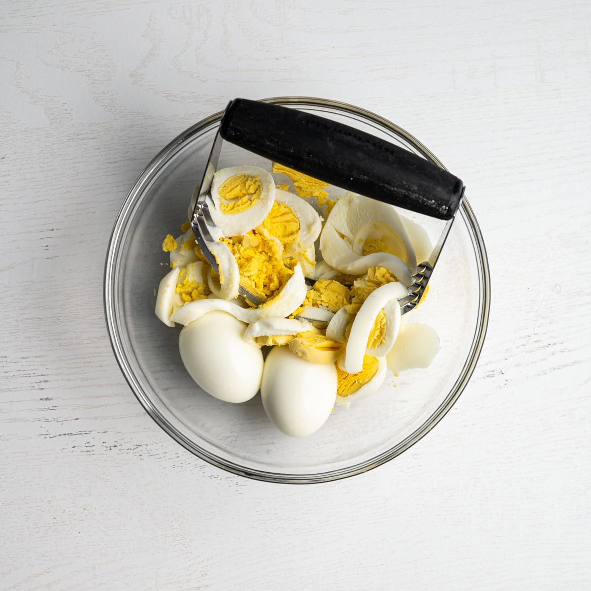 glass bowl with hard boiled eggs and a biscuit cutter chopping up eggs.