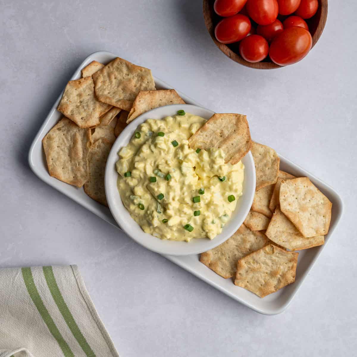 white tray of crackers with a small bowl of egg salad served with cherry tomatoes.