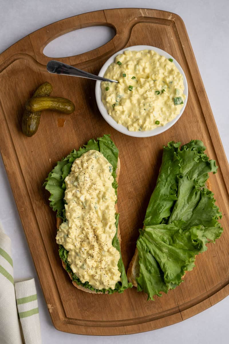 building an egg salad sandwich on a wooden board.
