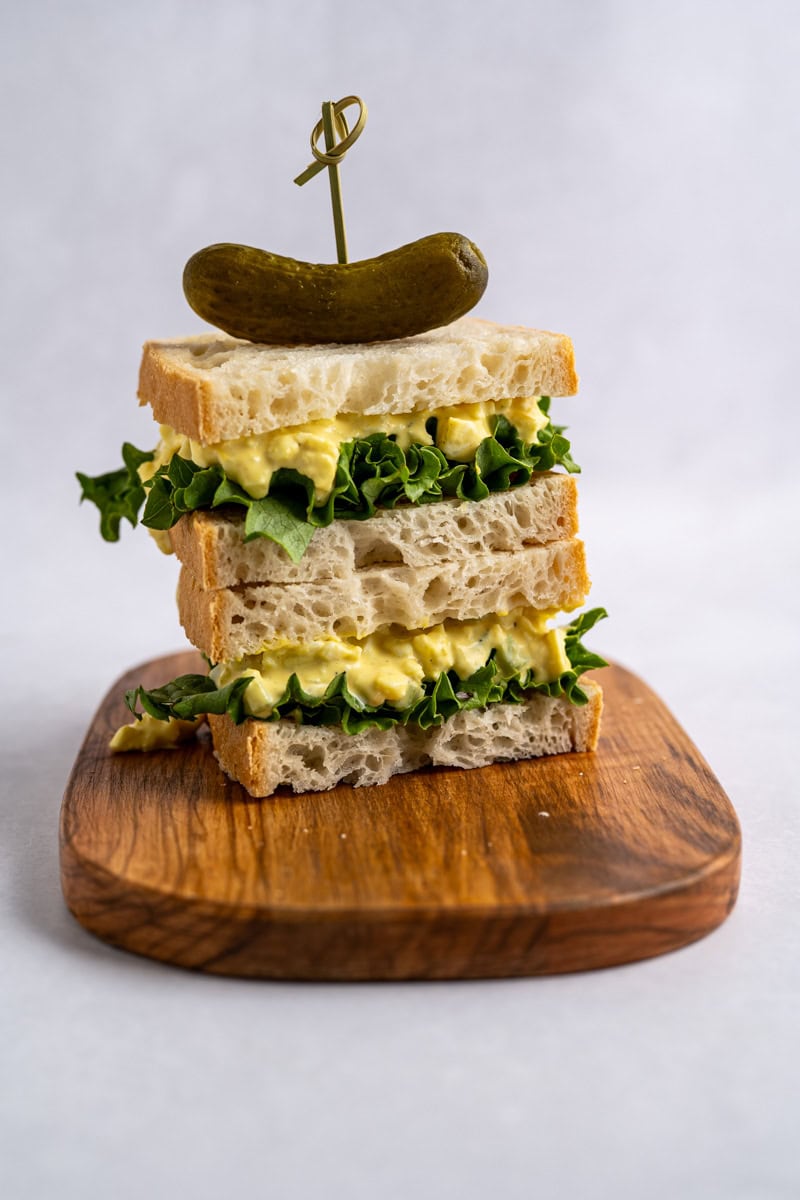 stacked egg salad sandwiches on a wooden board.