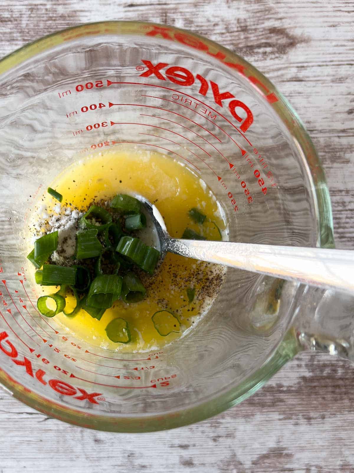 measuring cup with butter, green onion tops and spices.