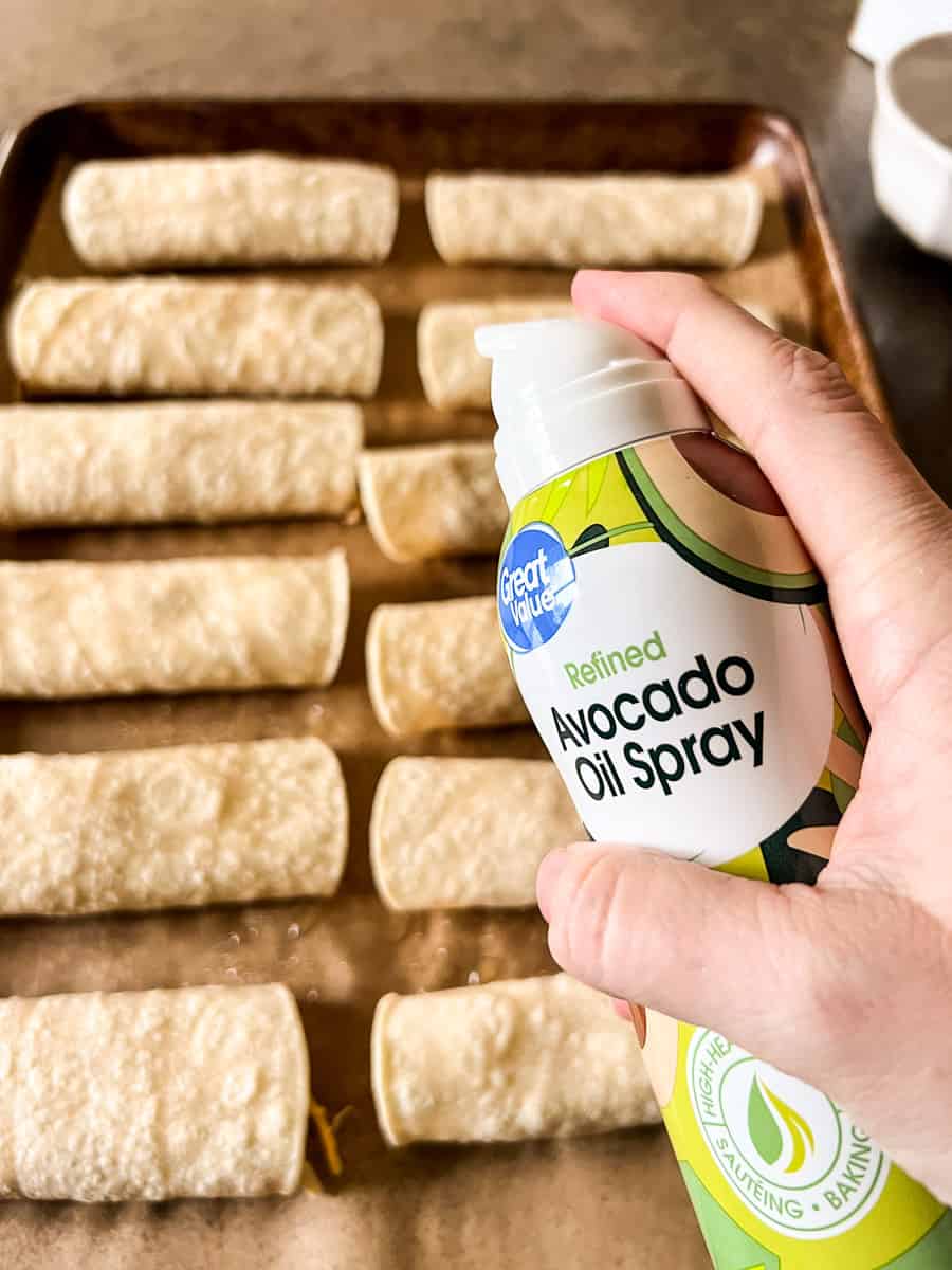 rolled flautas on cookie sheet being sprayed with avocado oil.