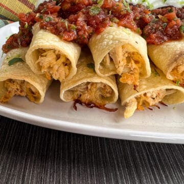 finished chicken flautas on a platter topped with salsa, guacamole and lime crema.