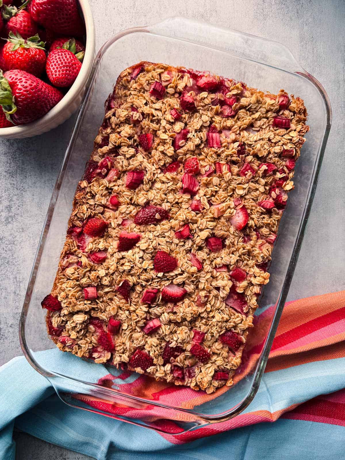 glass baking dish of strawberry rhubarb baked oatmeal with a bowl of strawberries.