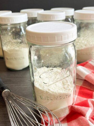 mason jars filled with pancake mix with a whisk and red and white checked napkin.