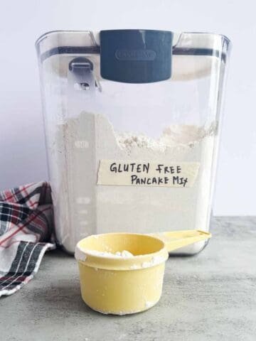 storage container full of pancake mix with a yellow measuring cup in front.