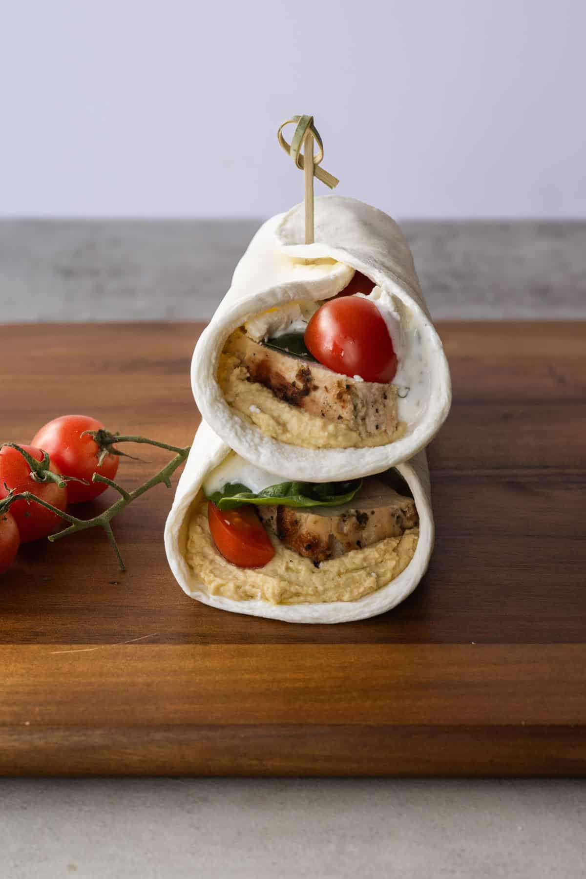 two hummus chicken wraps stacked on a wooden board held together with a toothpick.
