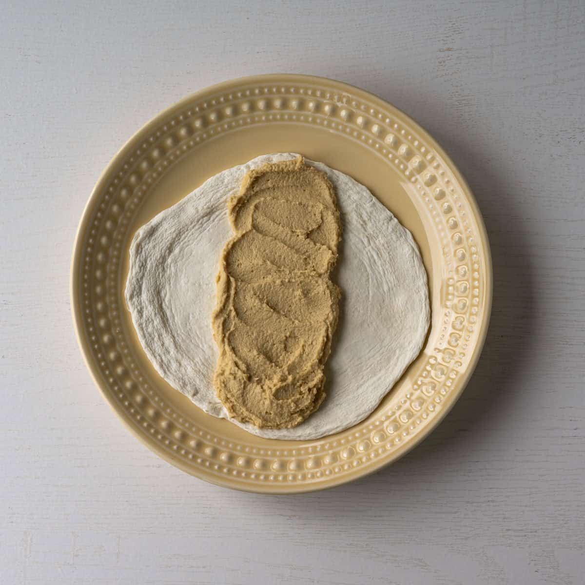 egg white wrap on a yellow plate with hummus down the middle.