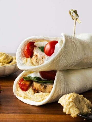stacked chicken hummus wraps on a wooden board.