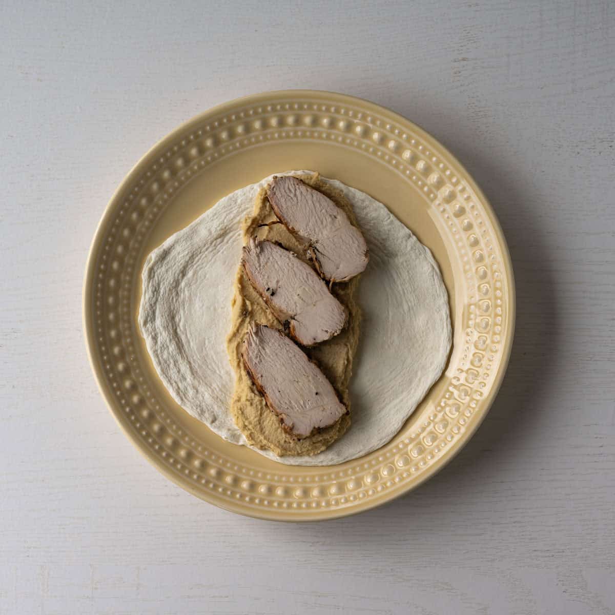egg white wrap topped with hummus and sliced chicken breast pieces.