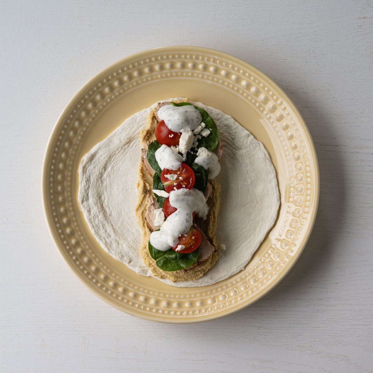 chicken hummus wrap drizzled with tzatziki sauce.