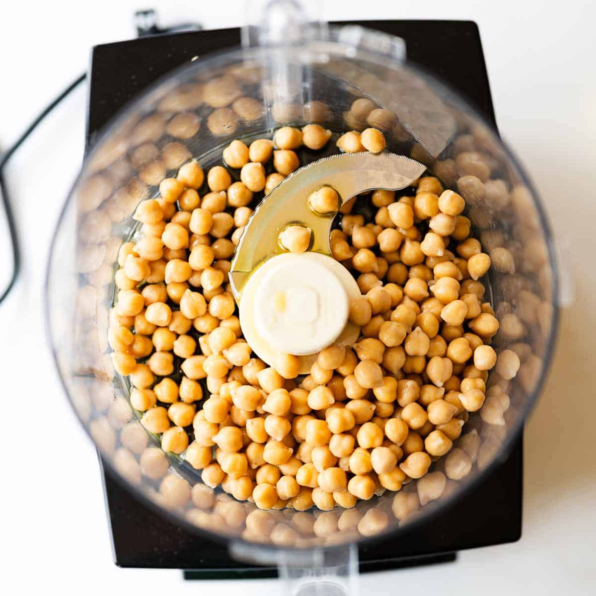 chickpeas and garlic infused olive oil inside a food processor bowl.