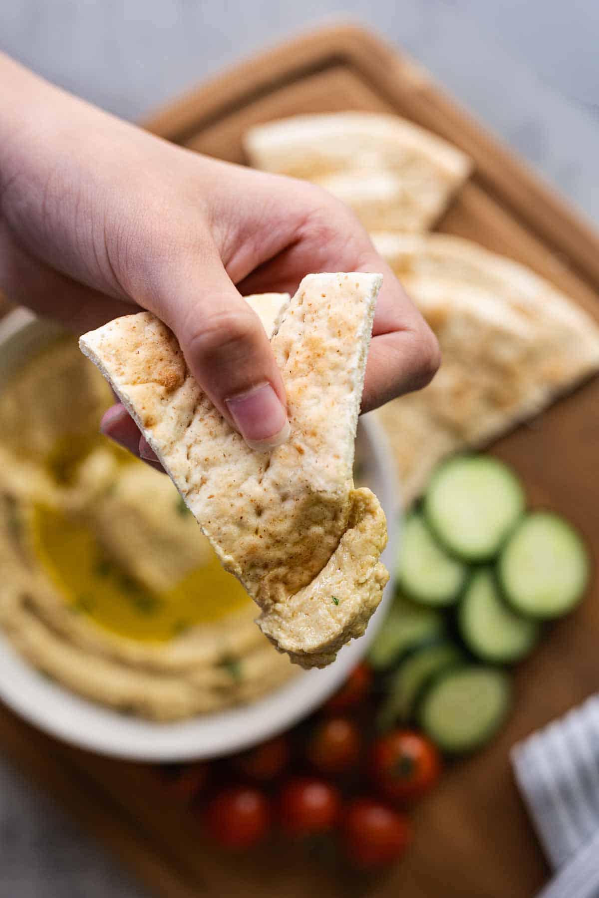 hand holding a pita dipped into hummus.