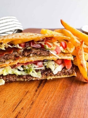 quesadilla burger cut in half and stacked next to french fries with a side of mexi ranch dressing all on a wooden board.