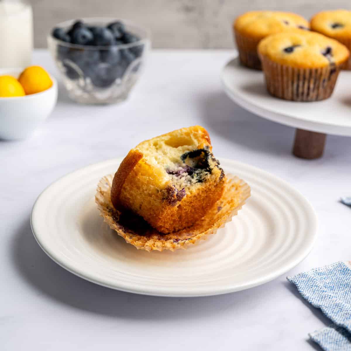 paper muffin liner peeled off blueberry muffin on a small white plate.