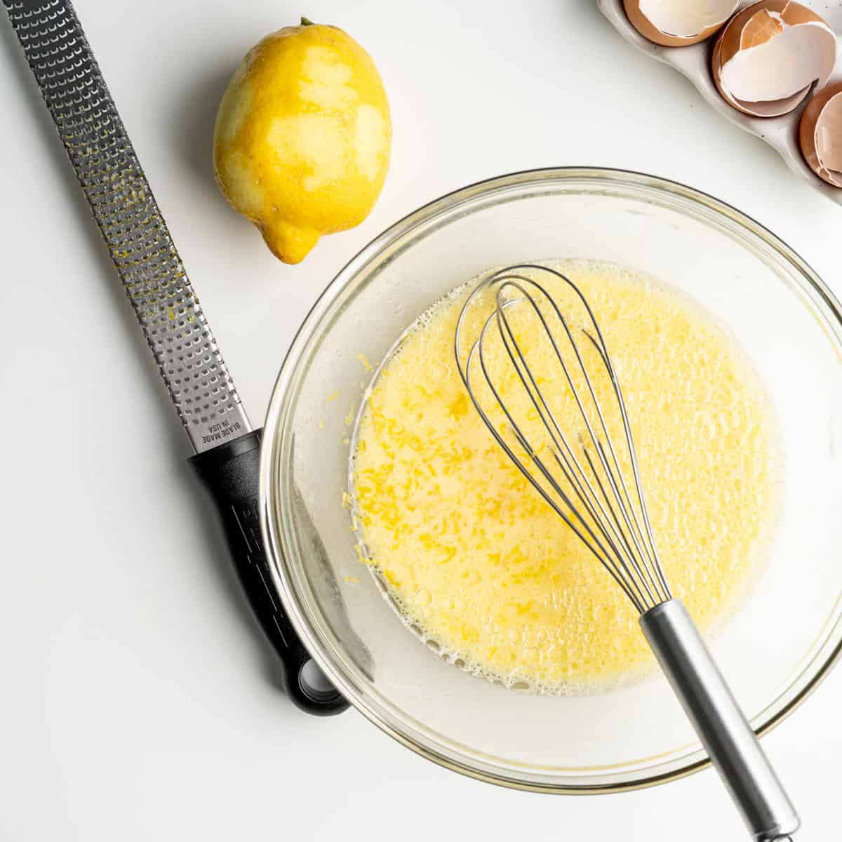 zested lemon with a microplane next to a bowl of wet ingredients to make muffins.