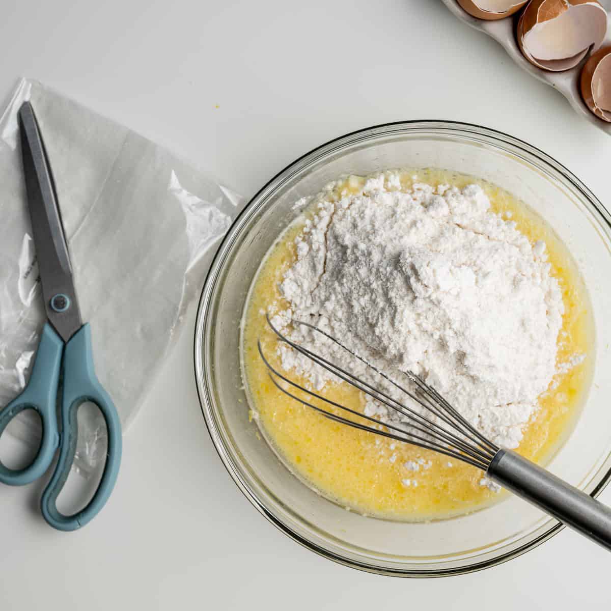 add the cake mix to the wet ingredients in the bowl alongside a whisk and a empty cake mix bag.