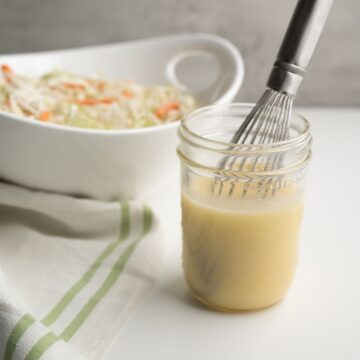 mason jar of dressing in front of a white bowl of chopped veggies.