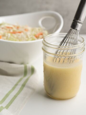mason jar of dressing in front of a white bowl of chopped veggies.