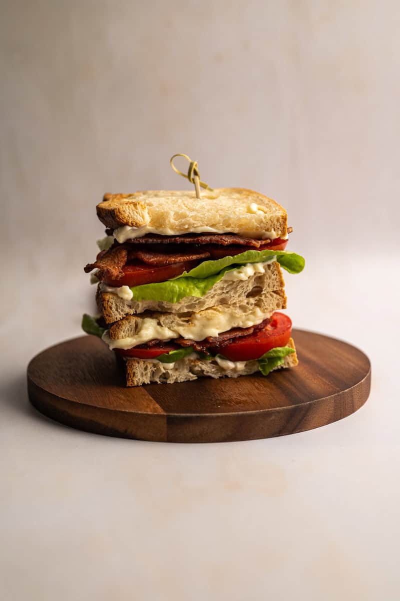 stacked BLT sandwich on a wooden board.