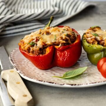 two stuffed peppers on a white plate with fresh basil and cherry tomatoes.