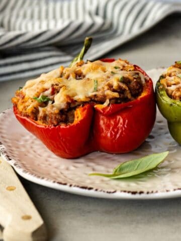 two stuffed peppers on a white plate with fresh basil and cherry tomatoes.