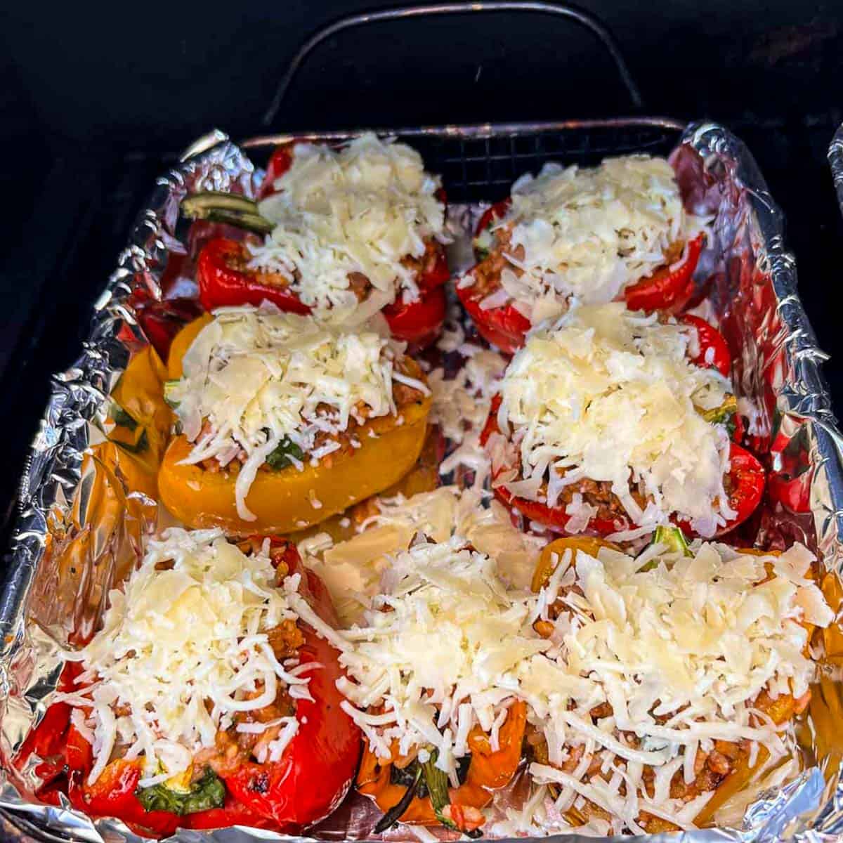 stuffed halved bell peppers topped with cheese in a grill basket on a grill.