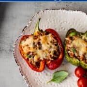 two stuffed bell pepper halves on a white plate with fresh basil and cherry tomatoes.