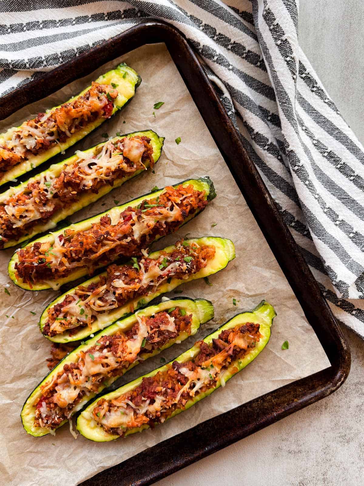 six stuffed zucchini halves on a baking sheet.