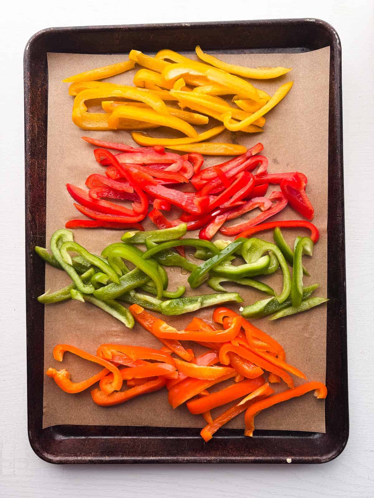 variety of colored bell peppers cut in strips and placed on a baking sheet.