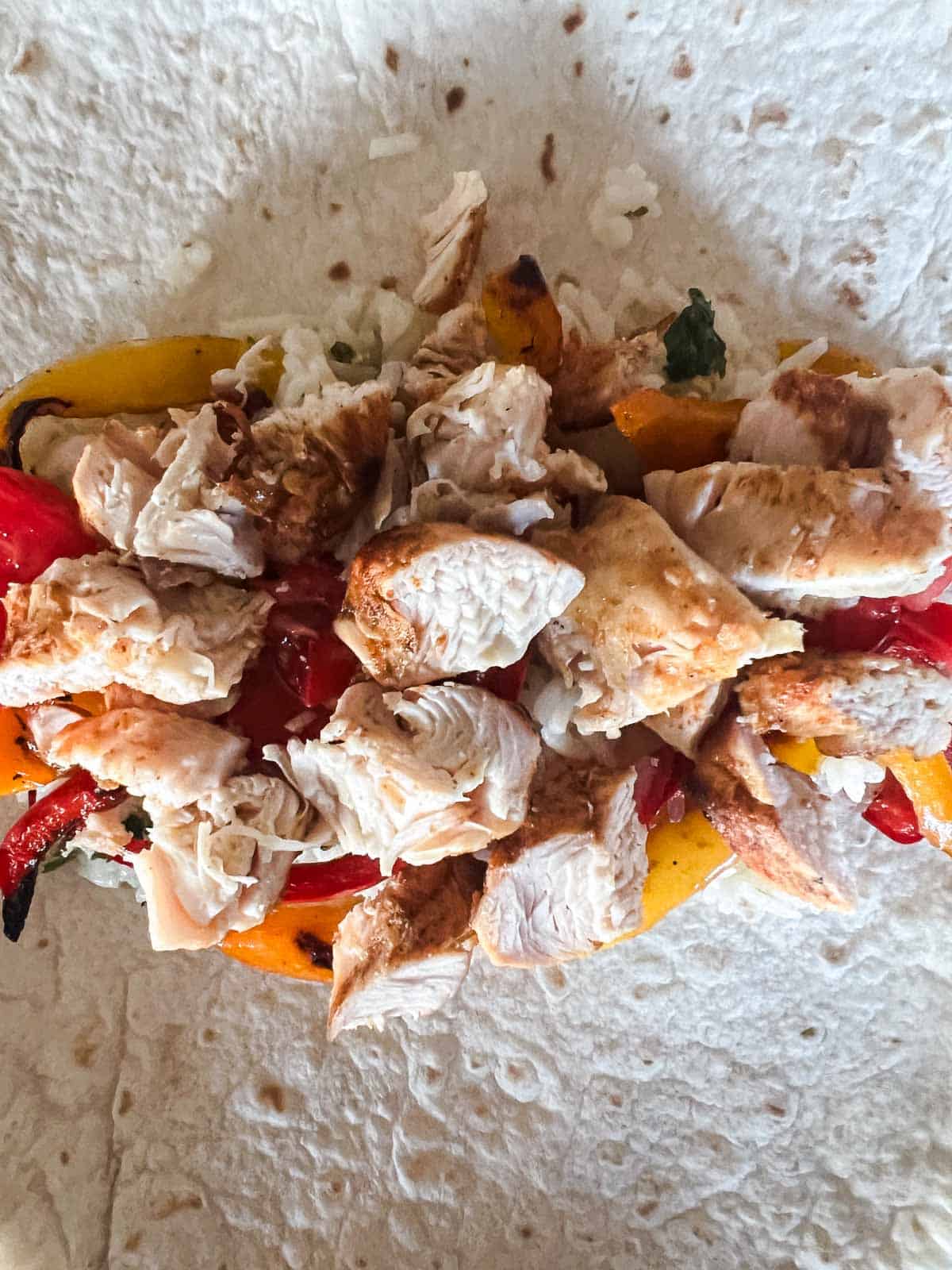 in the center of a tortilla is rice, peppers, tomatoes and diced chicken.