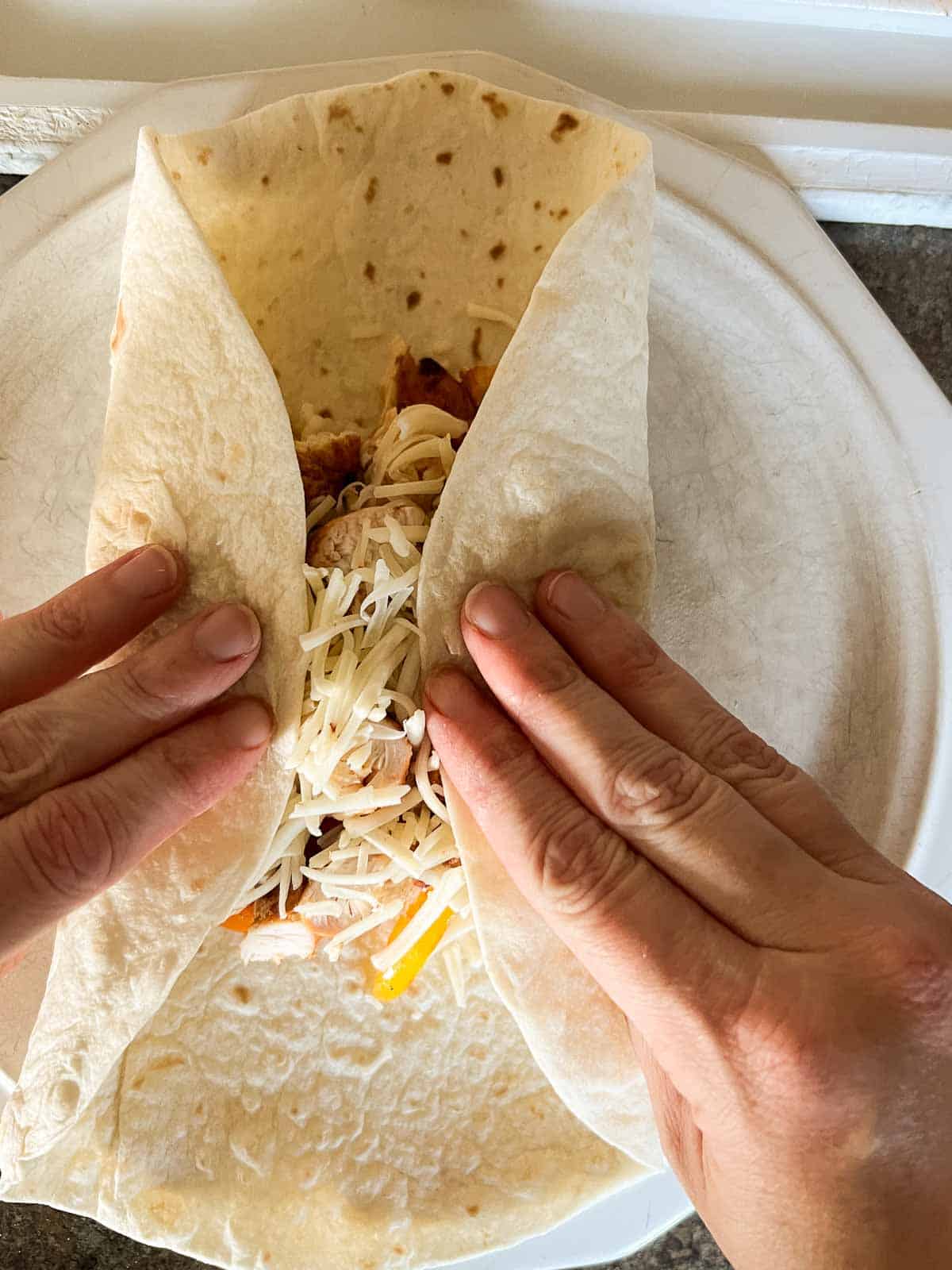 two hands rolling a burrito.