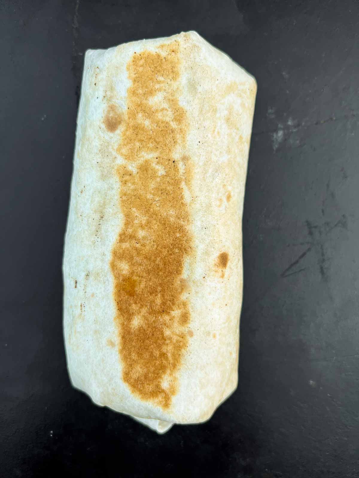 golden brown burrito cooking on a blackstone flat top.