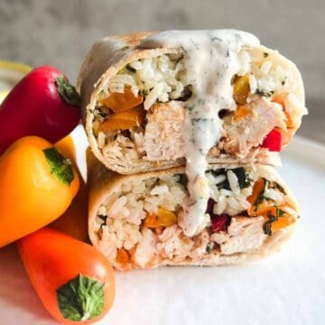 chicken burrito halved, stacked and drizzled in ranch dressing while sitting on a plate.