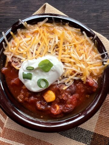 bowl of chili topped with shredded cheese, sour cream and green onions.