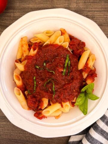 white bowl filled with penne pasta topped with pasta sauce, and chopped basil.