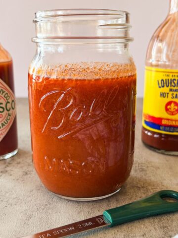 mason jar of buffalo sauce with two bottles of hot sauce in the background.
