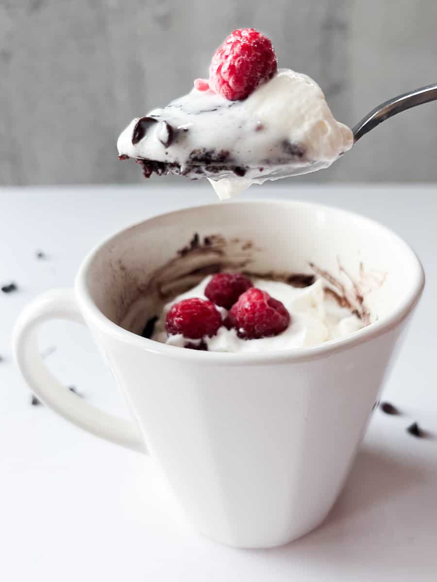 mug with a spoon filled with cake, whipped cream and raspberries.