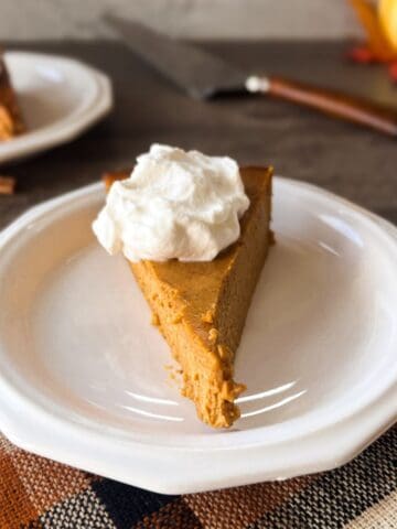 a slice of pumpkin pie topped with whipped cream on a small white plate.