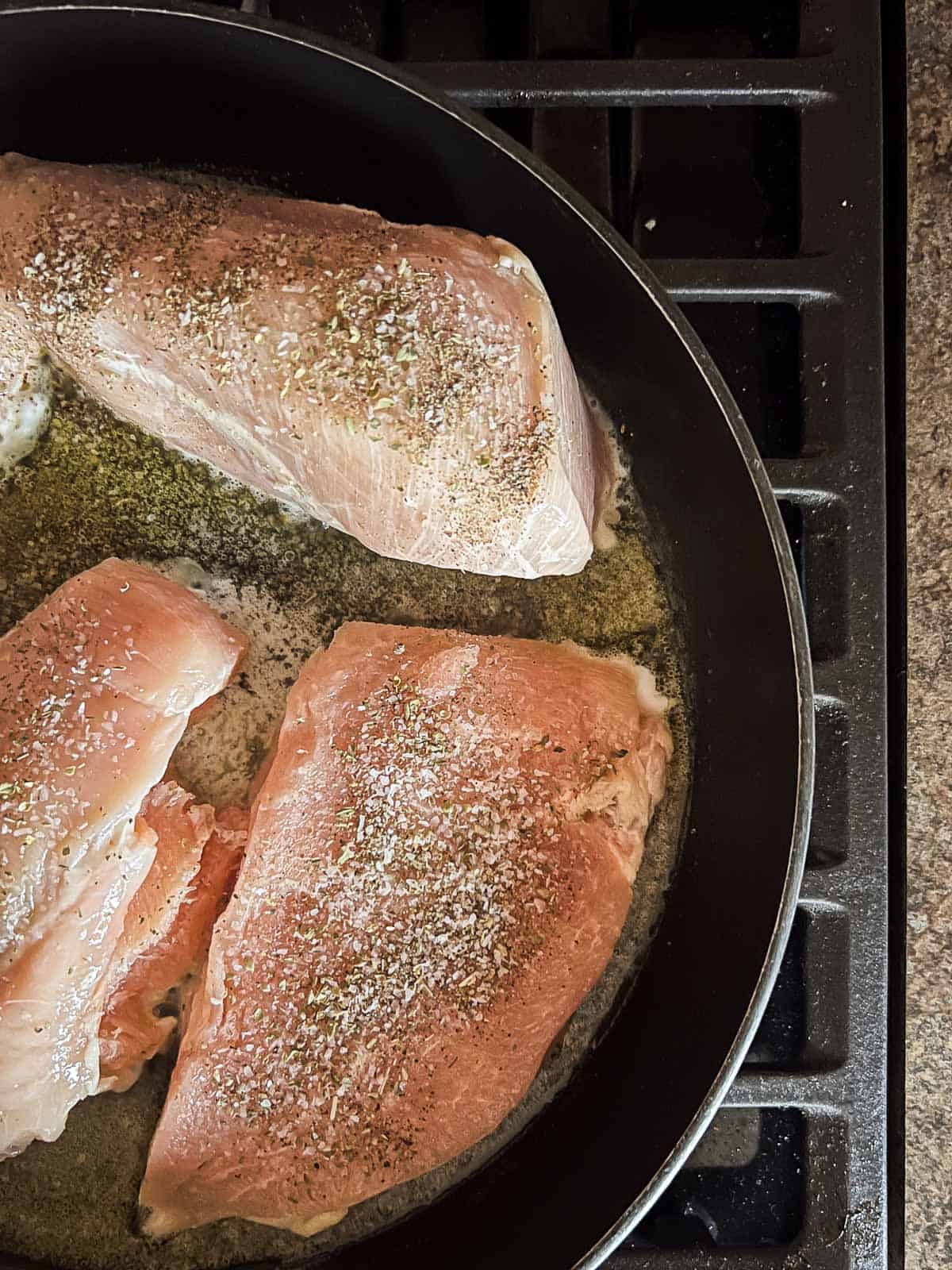 chicken breasts in a skillet sprinkled with spices.