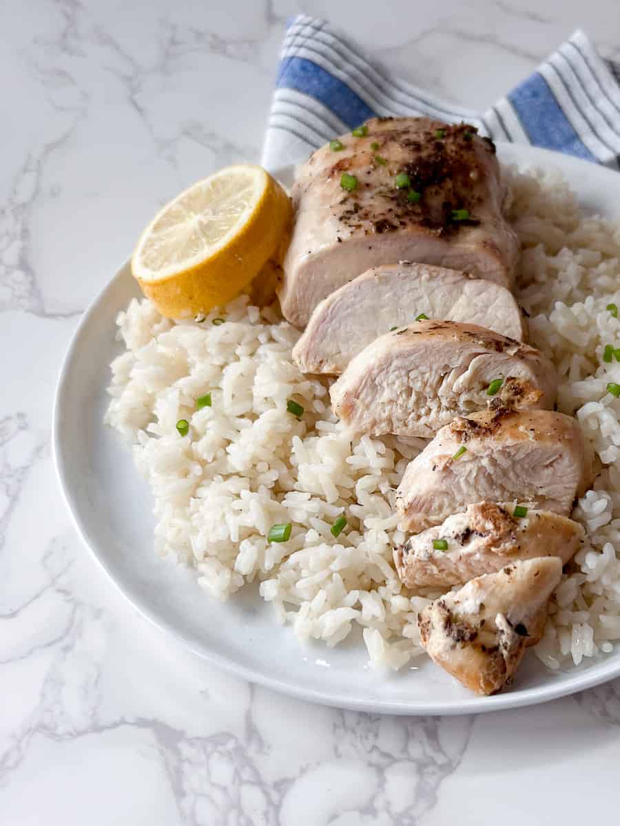 sliced chicken breast on top of white rice and a lemon slice.