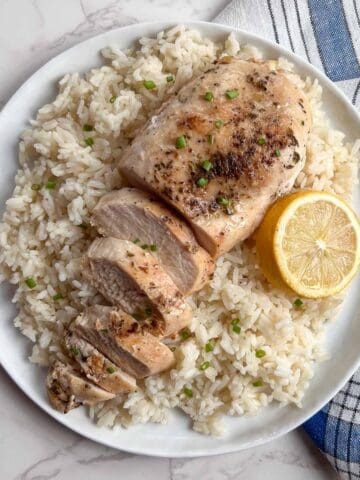 sliced chicken breasts on a bed of rice with a lemon slice.