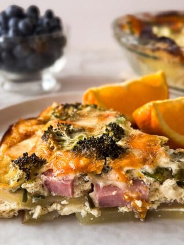 slice of quiche on a white plate with orange slices and blueberries.