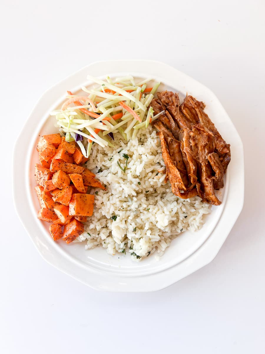 white bowl filled with rice, pulled pork, sweet potatoes, broccoli slaw.