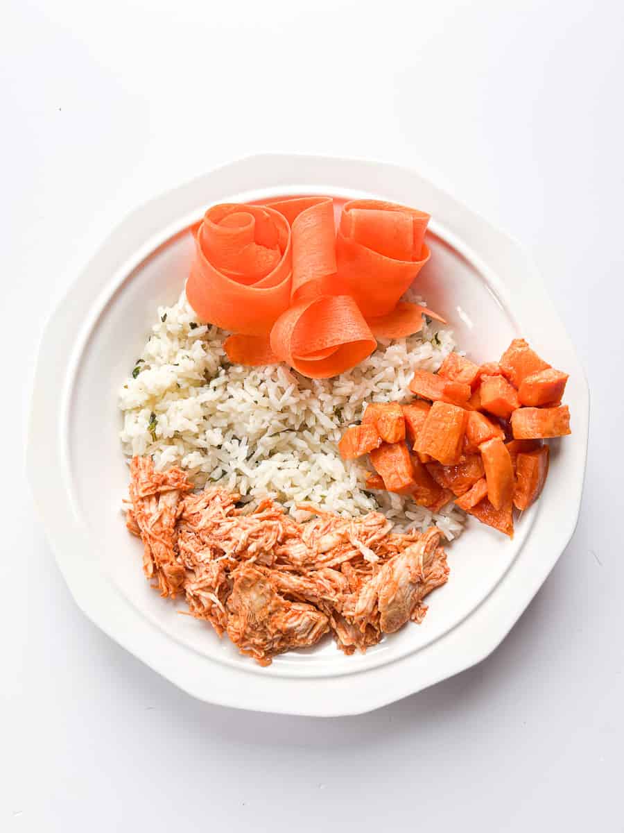 white bowl with cilantro lime rice, buffalo chicken,  carrots, and roasted sweet potatoes.