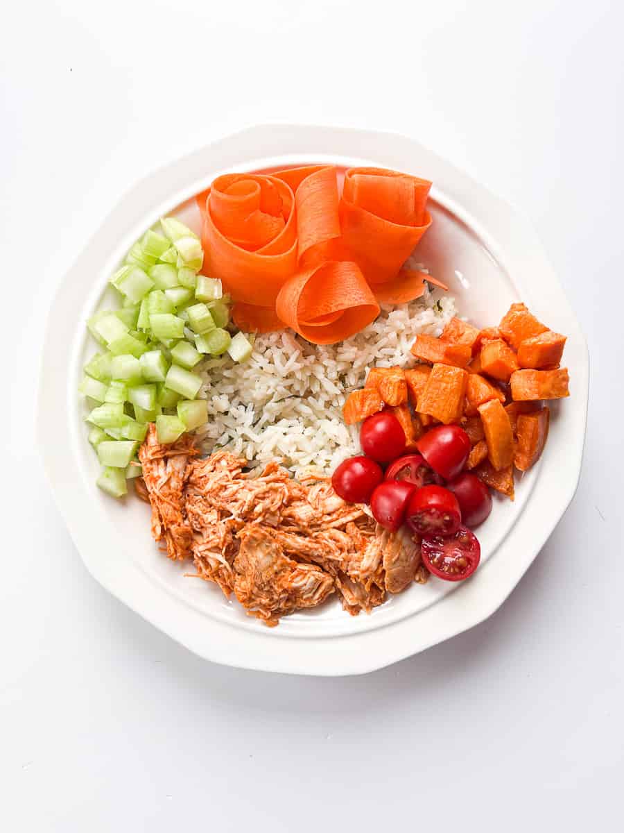 white bowl with cilantro lime rice, buffalo chicken,  carrots, roasted sweet potatoes and tomatoes.