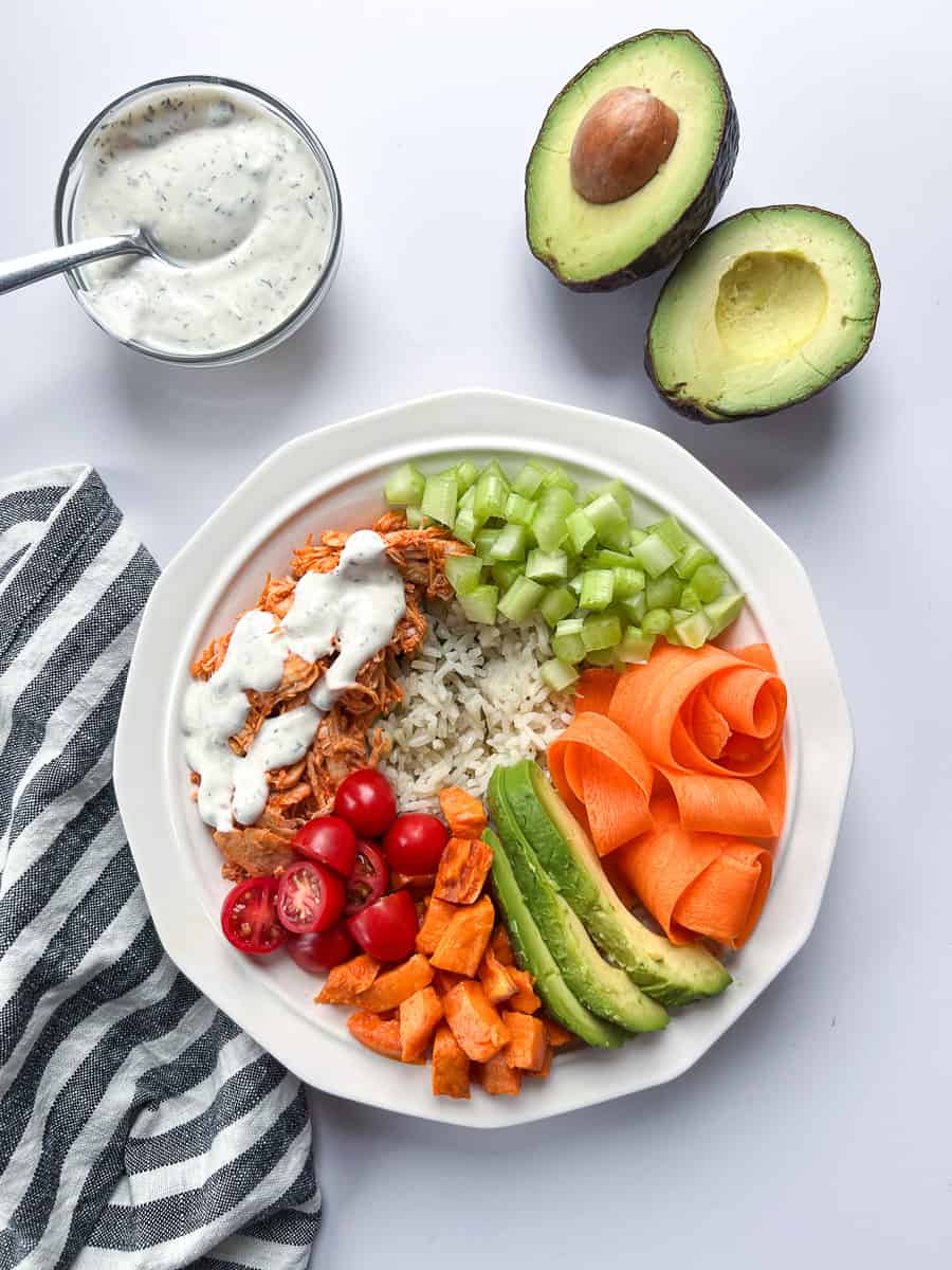 rice bowl in a white bowl with an avocado cut in half and a small bowl of ranch with a spoon.